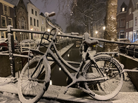 900632 Afbeelding van een besneeuwde fiets tegen de balustrade van de Magdalenabrug over de Nieuwegracht te Utrecht, ...